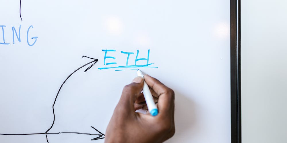 A hand writes the word ETH with a marker on a blackboard